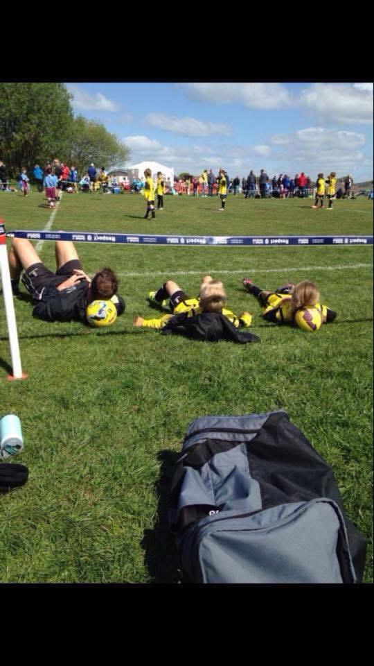 Coach and two young substitutes relaxing on footballs while watching the game together